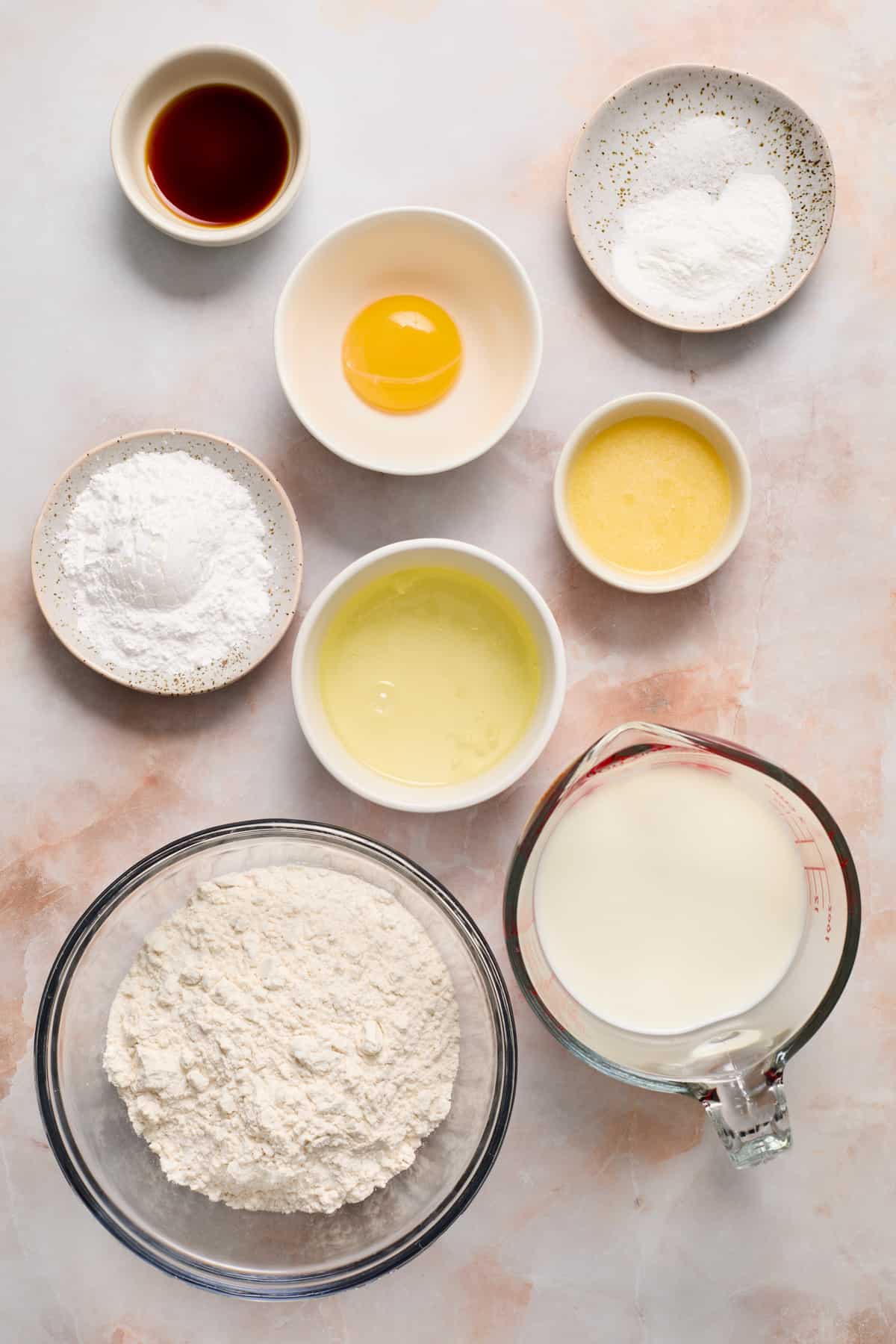 Flour, milk, eggs, vanilla and other ingredients to arranged on surface.