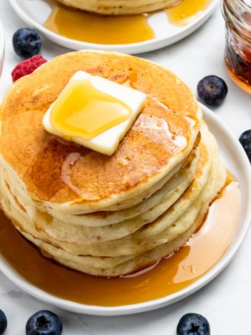 Stack of pancakes with maple and butter on white plate.