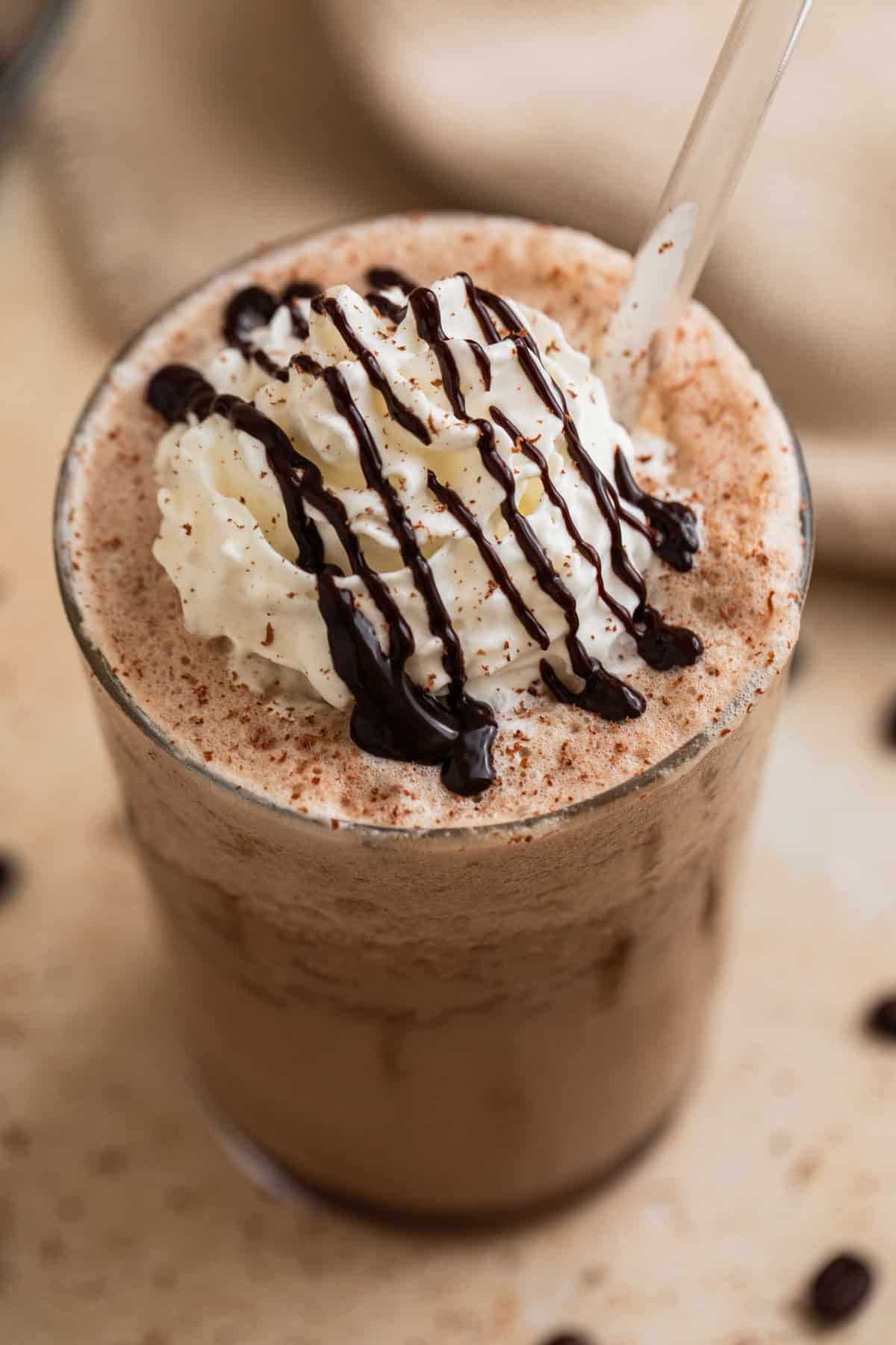 Mocha frappuccino in glass with whipped cream and chocolate drizzle on top.
