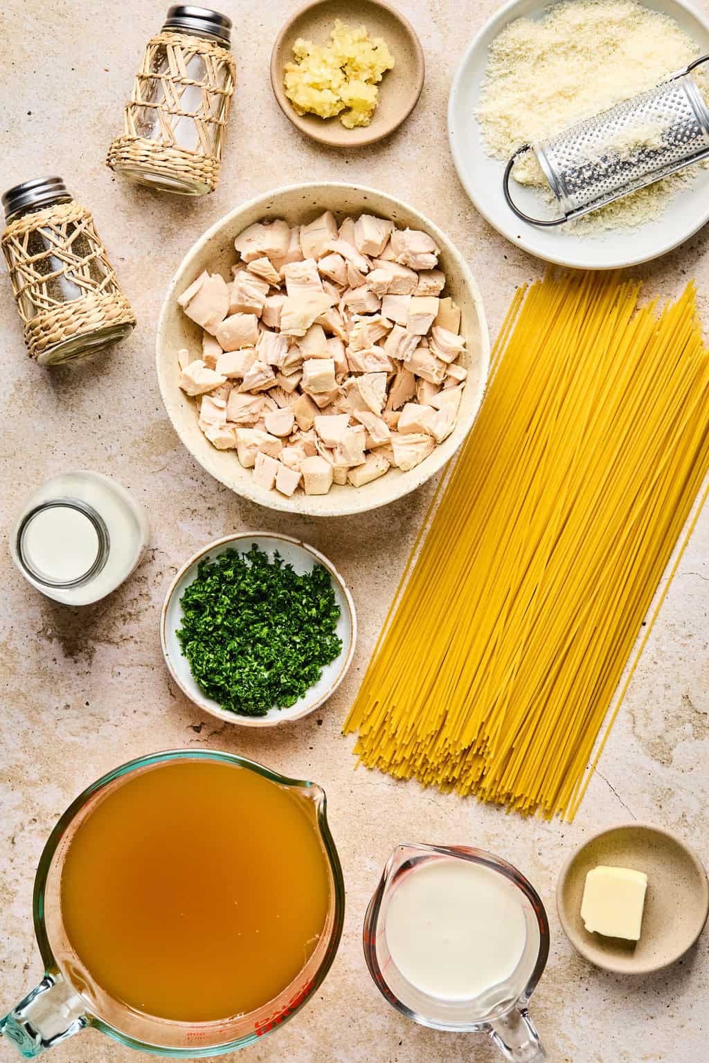Pasta, chicken cubed, broth, parsley and other ingredients arranged on surface.