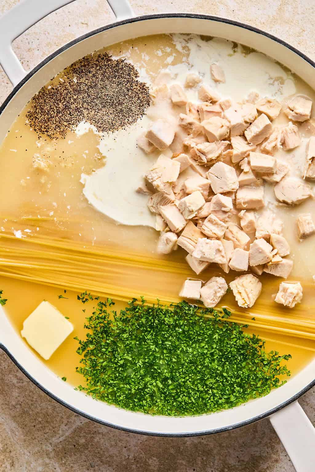 Pot with dried pasta, butter, chicken, parsley, cream, and spices.