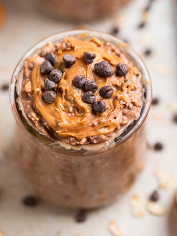 Chocolate chip and peanut butter topped chocolate overnight oats in glass with spoon beside it.