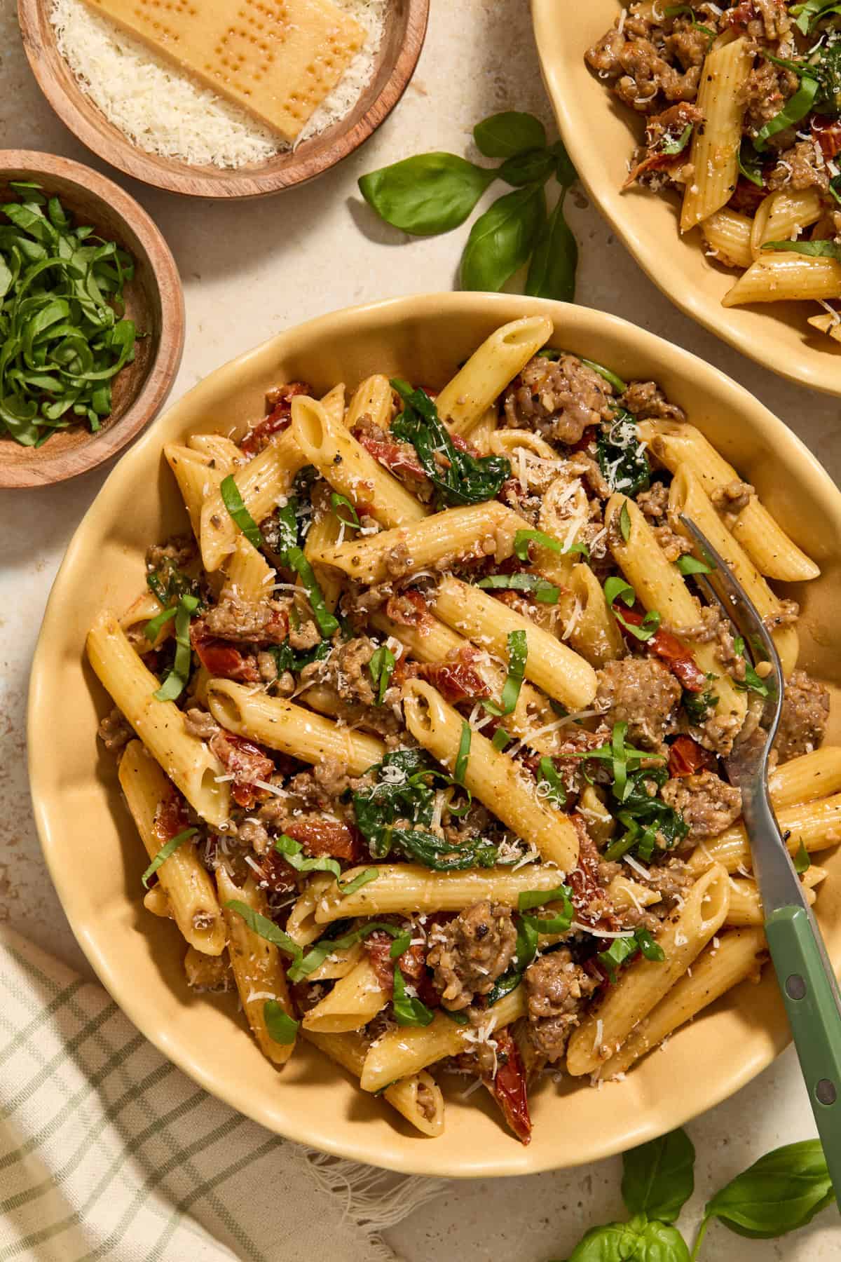 Plate with serving of sun-dried tomato pasta with Italian sausage topped with chopped basil.