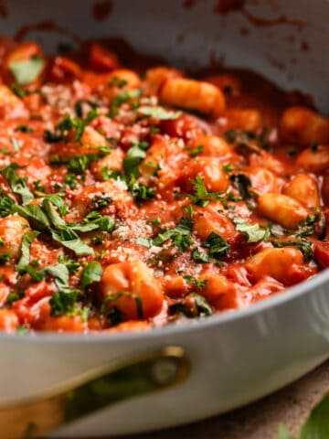 Creamy tomato basil skillet gnocchi topped with chopped basil and parsley.
