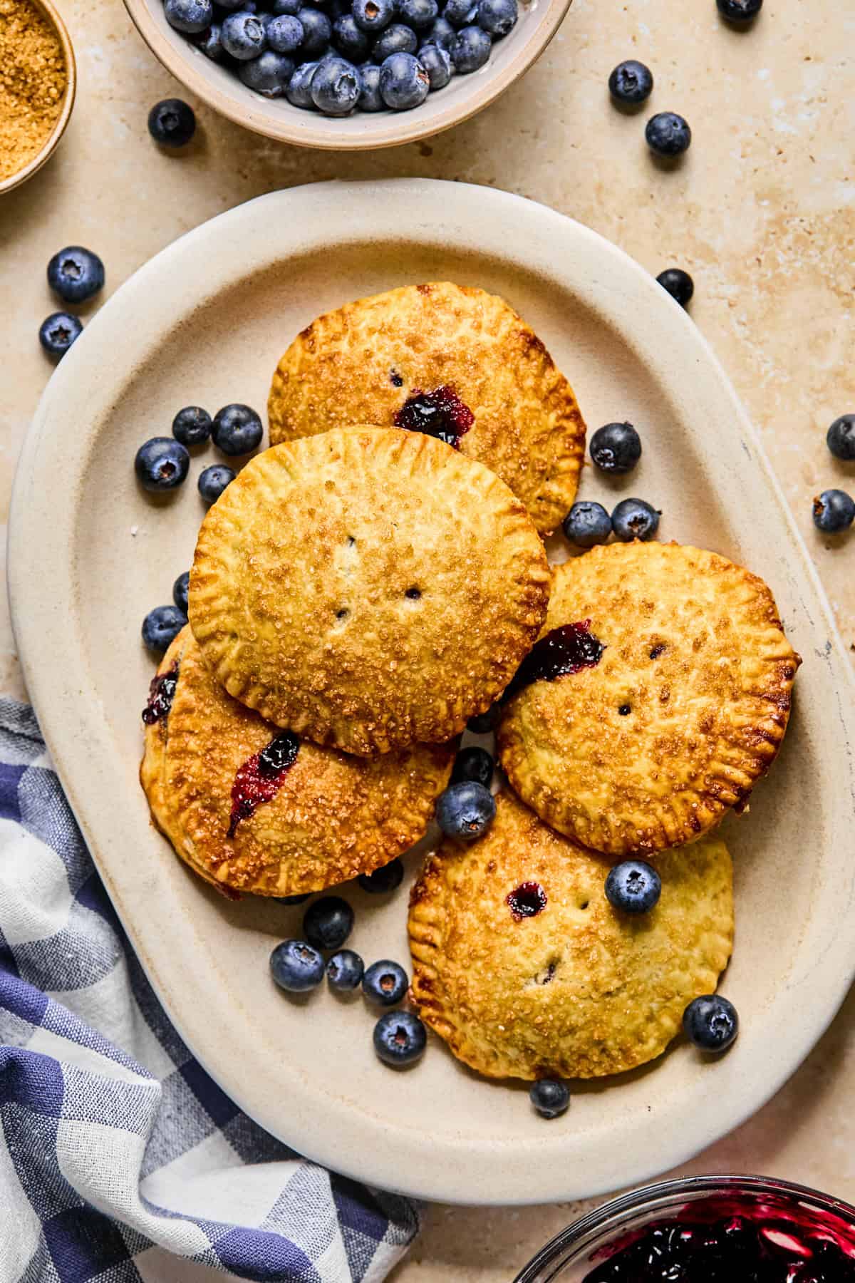Blueberry hand pies on plate with bowl of blueberries beside it.
