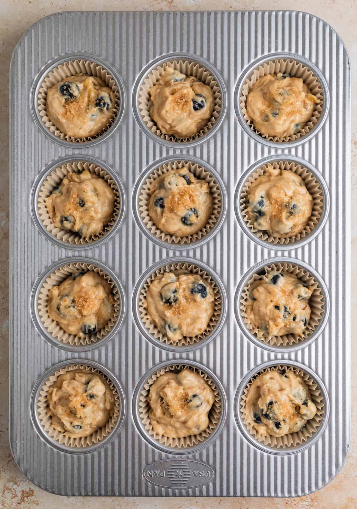 Blueberry banana muffin batter scooped into muffin tin before baking.
