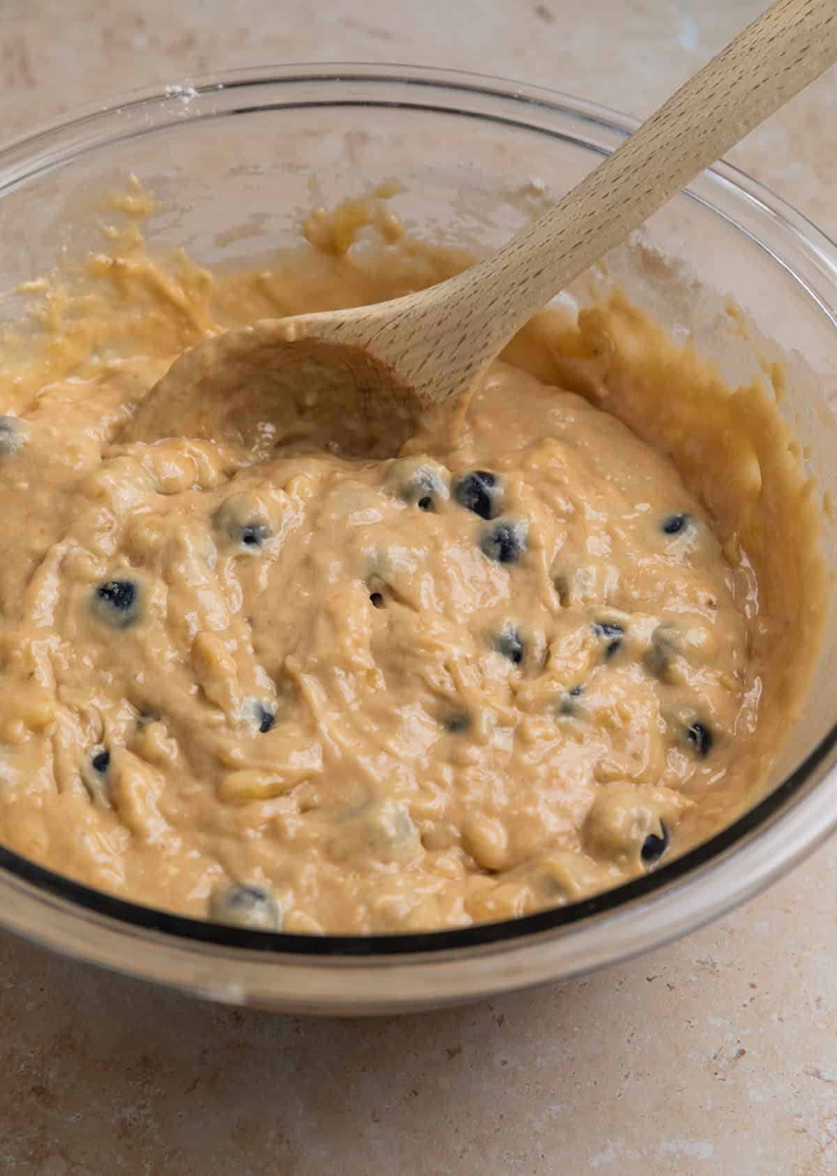 Prepared blueberry banana muffin batter in bowl with wood spoon.
