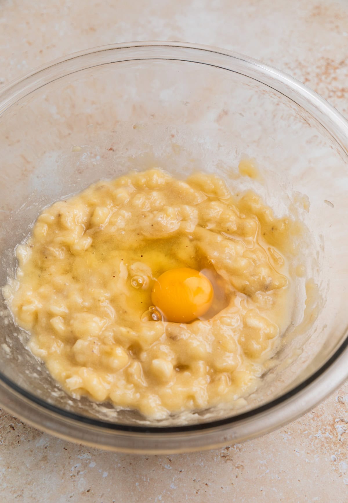Mashed banana in mixing bowl with egg in it before whisking.