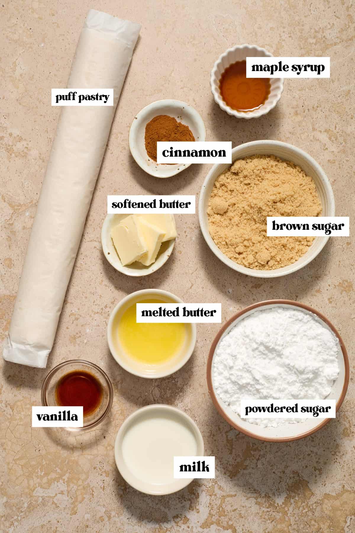 Puff pastry roll, brown sugar, cinnamon, butter and other labeled ingredients on surface.