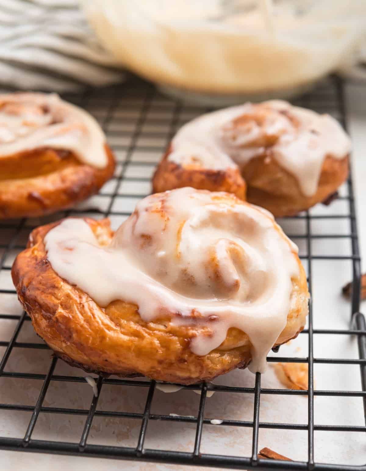 Puff pastry cinnamon rolls with maple icing on cooling rack.