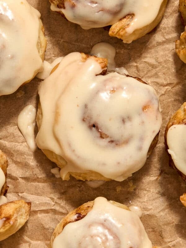 Maple icing topped puff pastry cinnamon rolls on parchment.