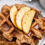 Stack of waffles with syrup and apples on white plate.