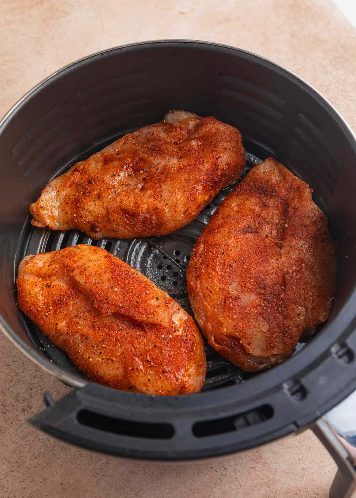 Seasoned chicken breast in air fryer basket.