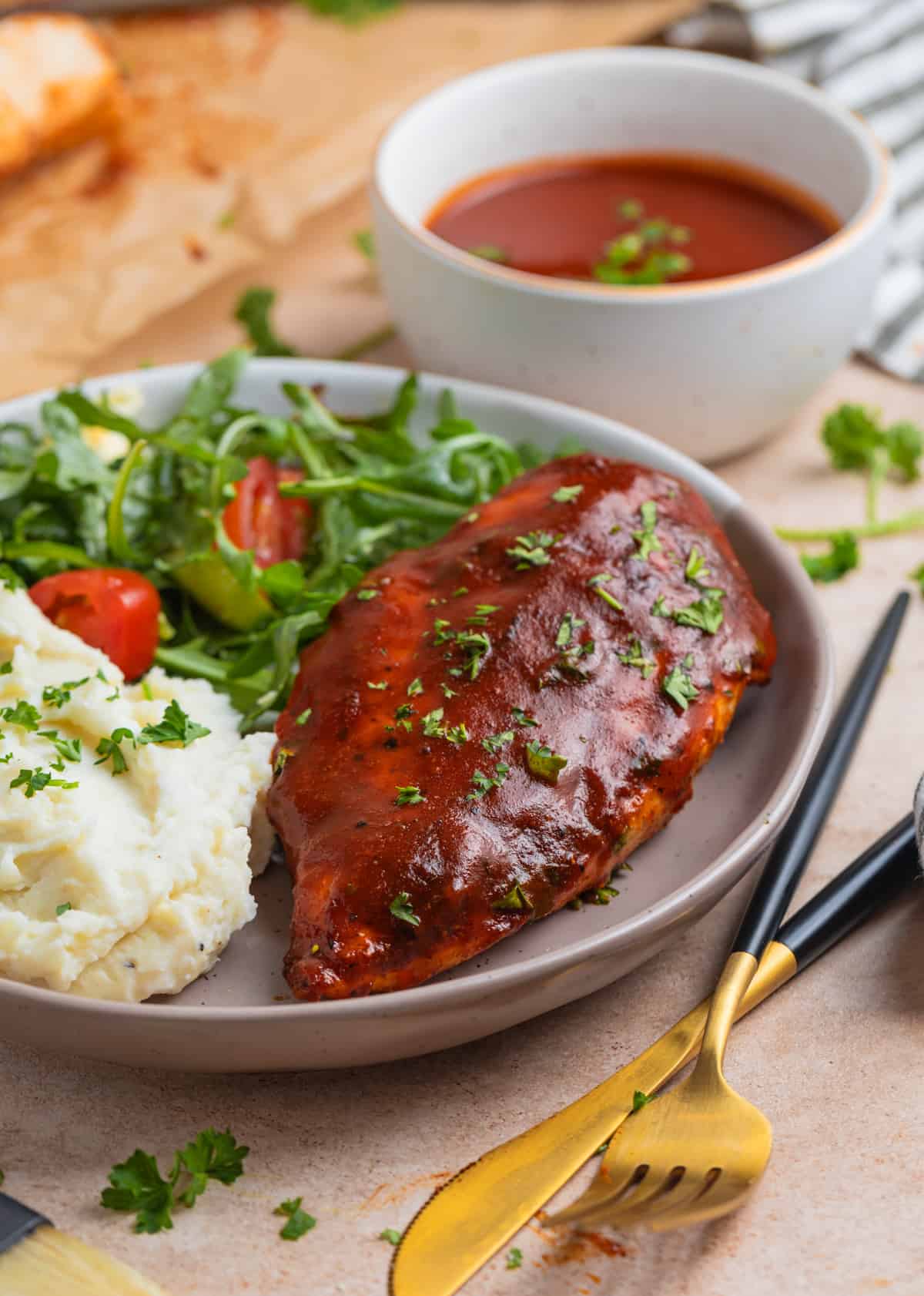 Plate with mashed potatoes, salad and BBQ chicken with fork and knife beside it.