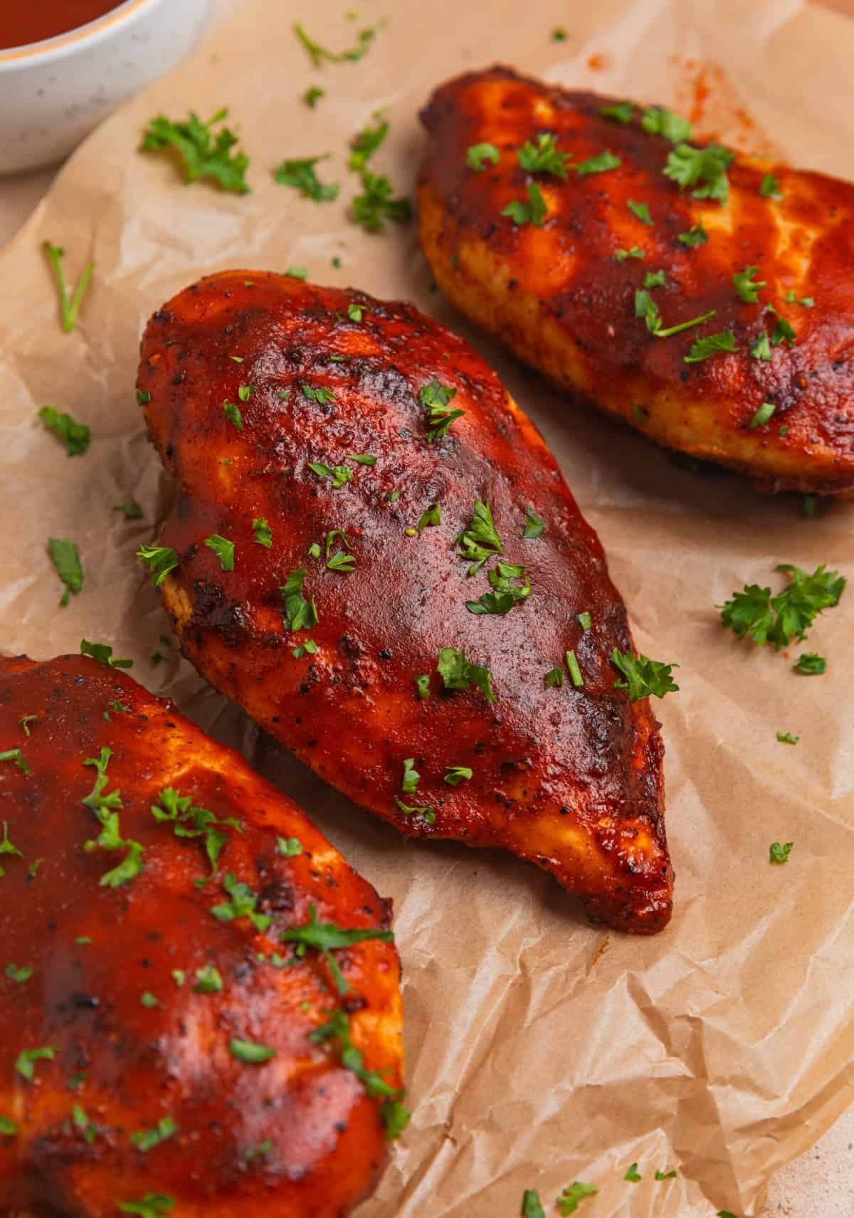 Air fryer BBQ chicken breasts on parchment topped with parsley.