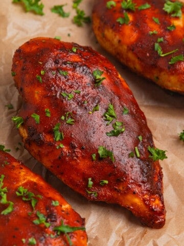 BBQ air fried chicken breasts arranged on parchment with chopped parsley.