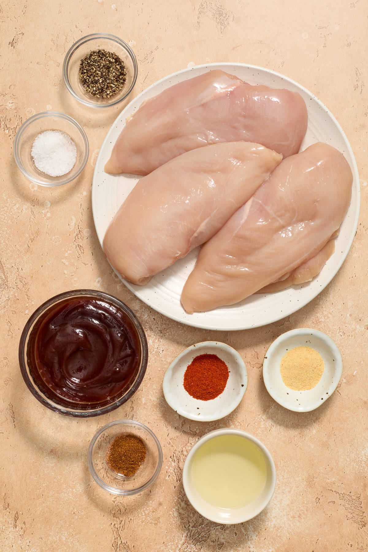 Raw chicken breasts, bbq sauce, seasoning and oil on surface.