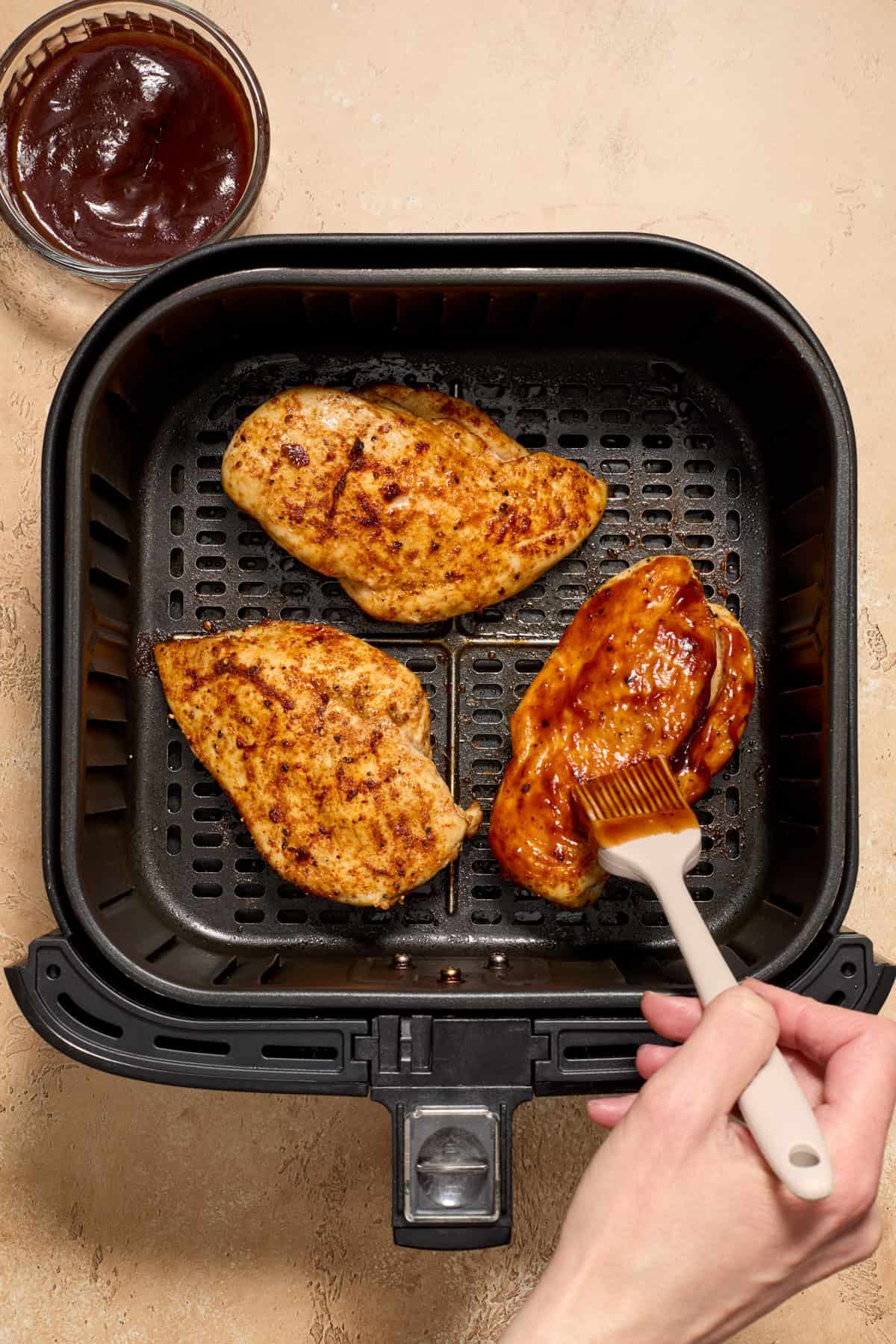 Air fryer basket with chicken with bbq sauce being brushed over top.