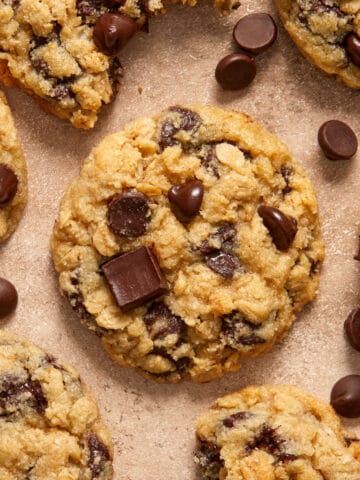 Oatmeal chocolate chip cookies arranged on surface with chocolate chips surrounding.