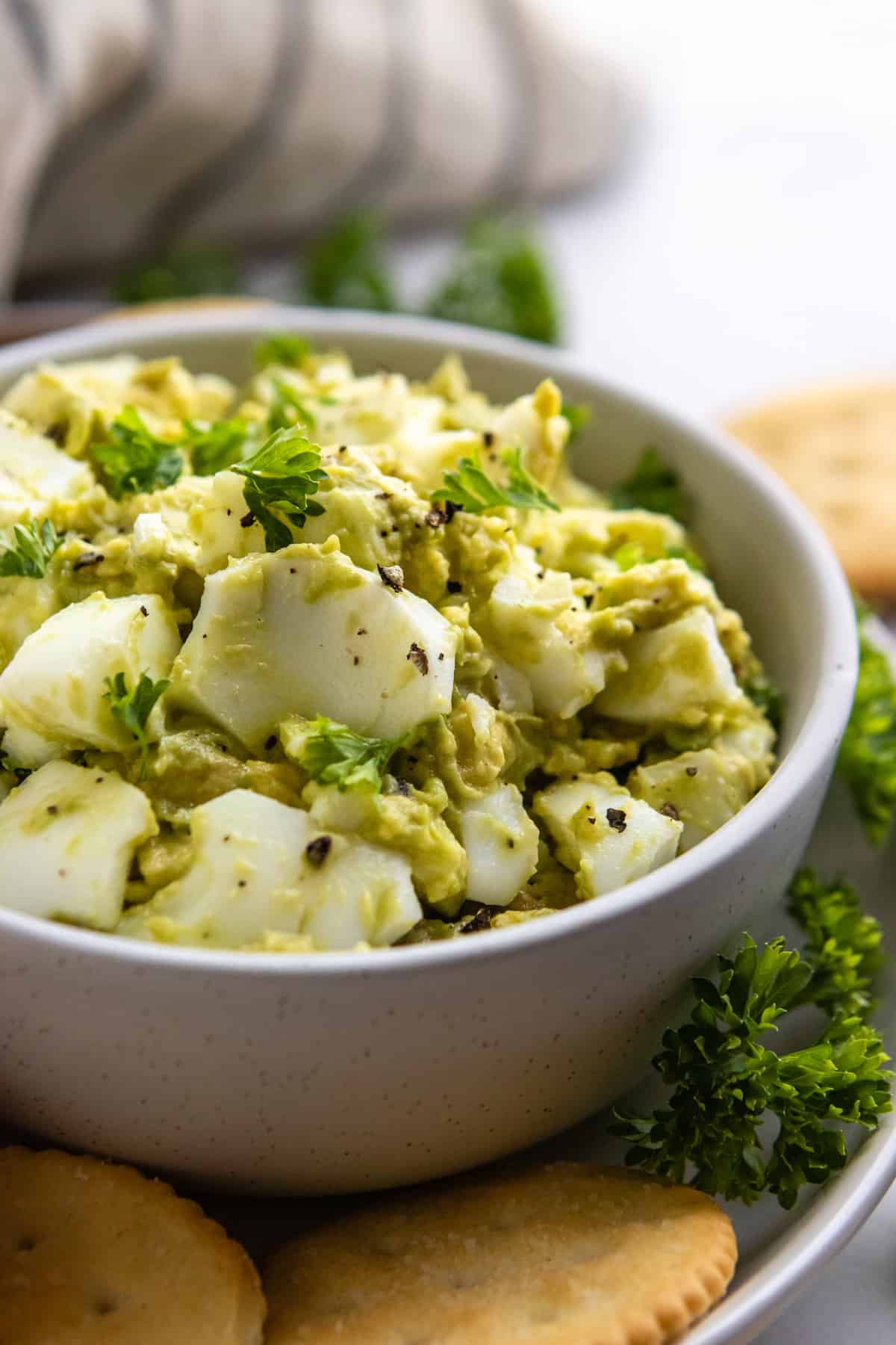 Avocado Egg Salad in bowl with crackers and fresh parsley.