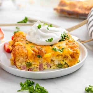 Breakfast casserole with tator tots on white plate with parsley and sour cream.
