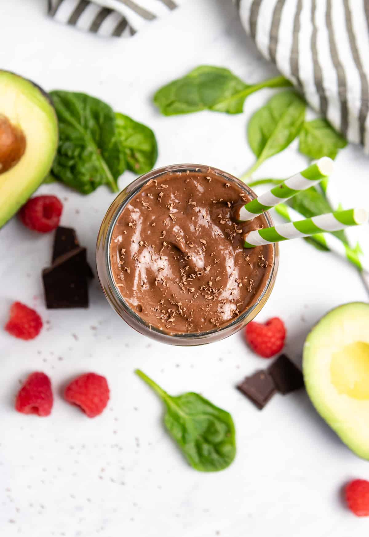 Overhead view of chocolate smoothie with spinach, avocado and raspberries next to it.
