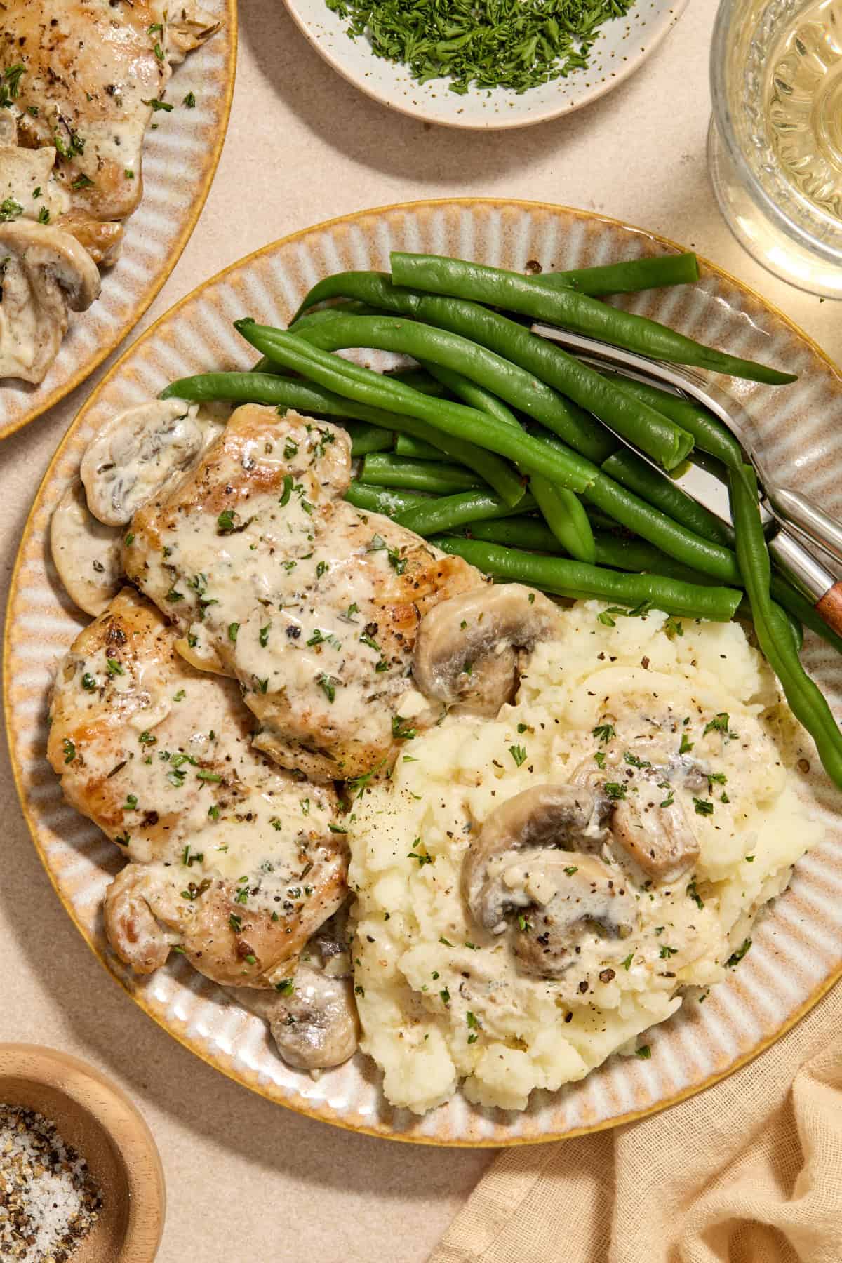 Cream plate with chicken thighs in creamy mushroom sauce and green beans and mashed potatoes.