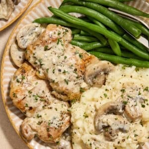 Plate with creamy chicken thighs and mushrooms with mashed potatoes and green beans.