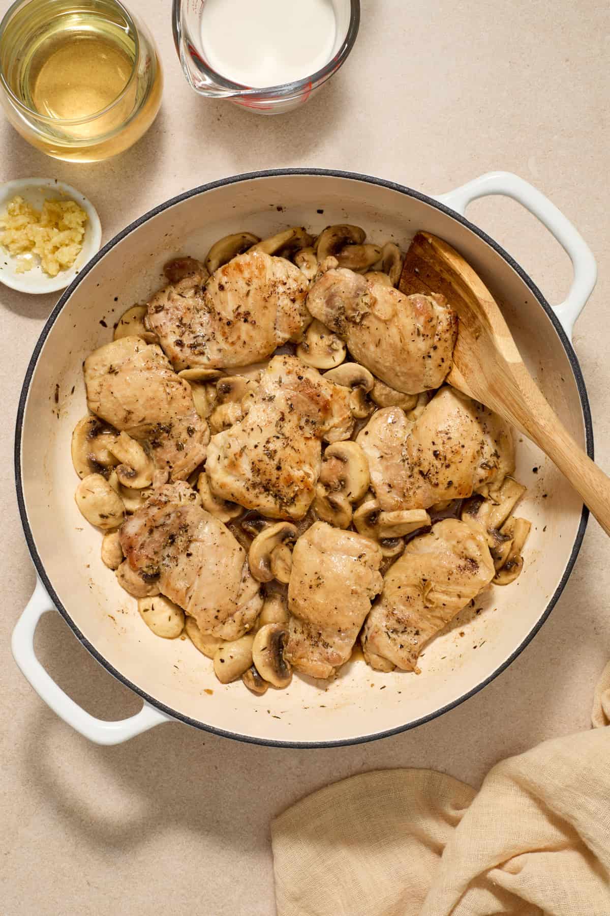 Mushrooms added to skillet with chicken thighs and wooden spoon propped in the pan.