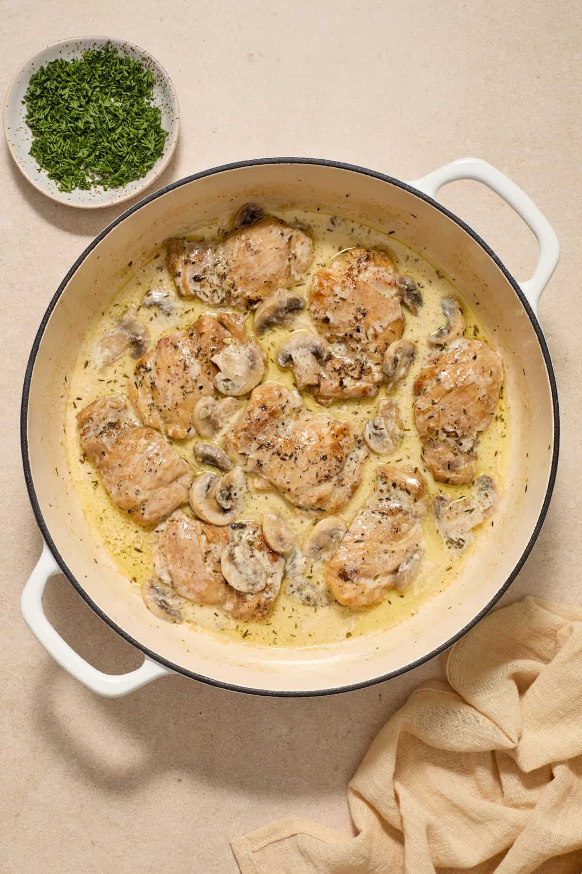 Cream added to chicken thighs and mushrooms in pan.