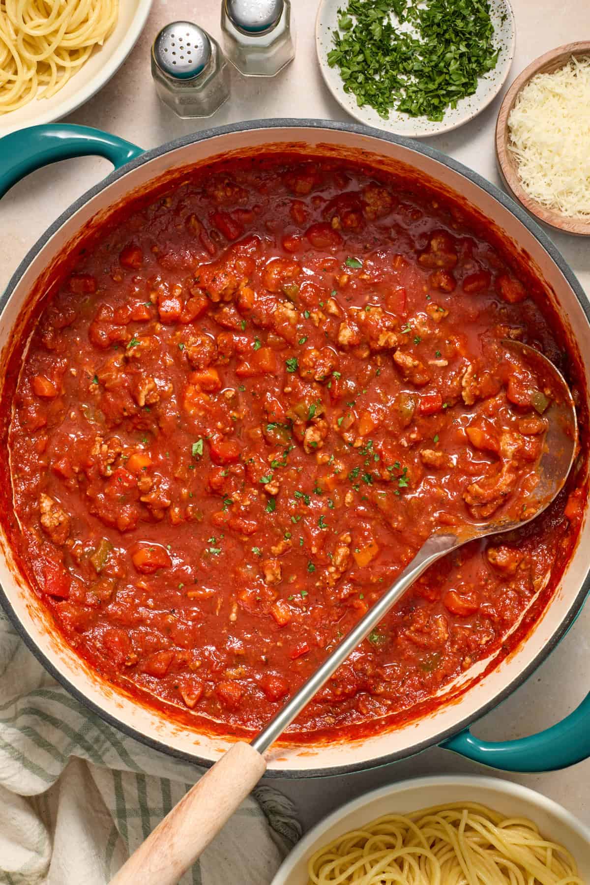 Ground turkey meat sauce in pot with ladle topped with parsley.