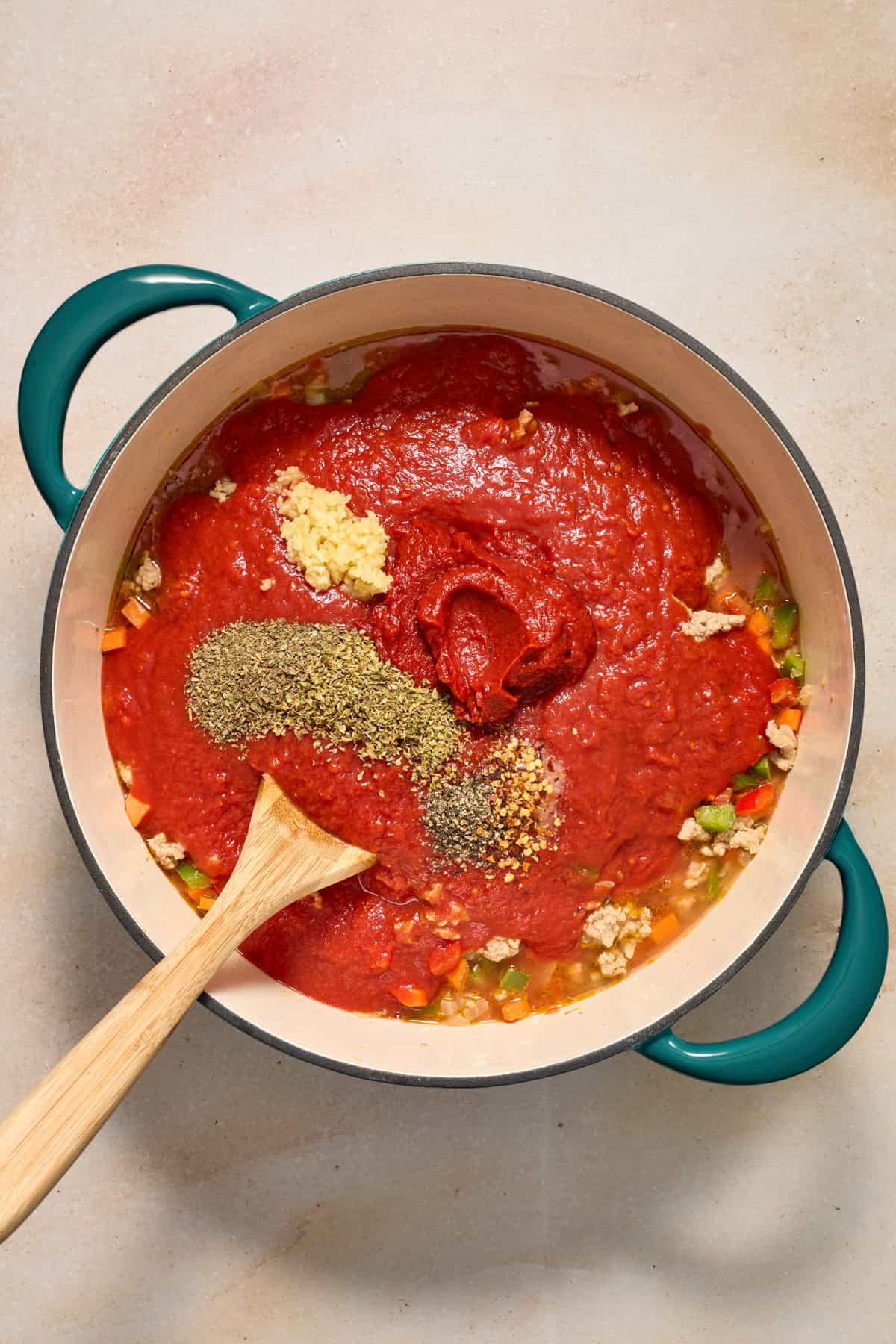 Crushed tomatoes, seasoning, garlic and other ingredients added to pot with meat and vegetables.