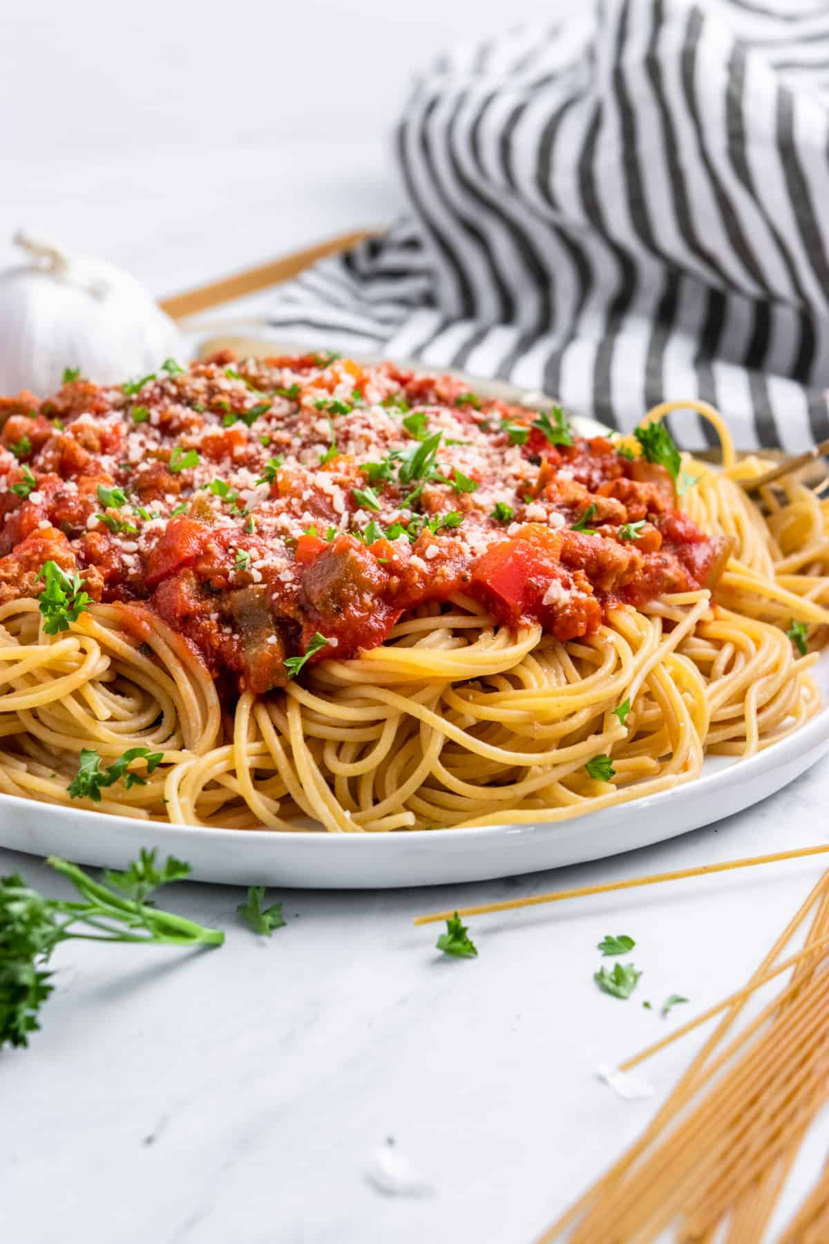 Plate of spaghetti with meat sauce and parmesan and striped napkin.