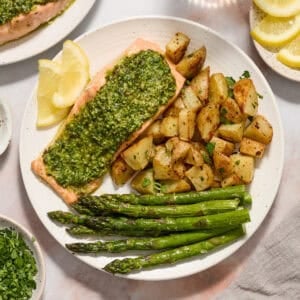 Pesto salmon dinner on white plate with potatoes, asparagus and two lemon slices.