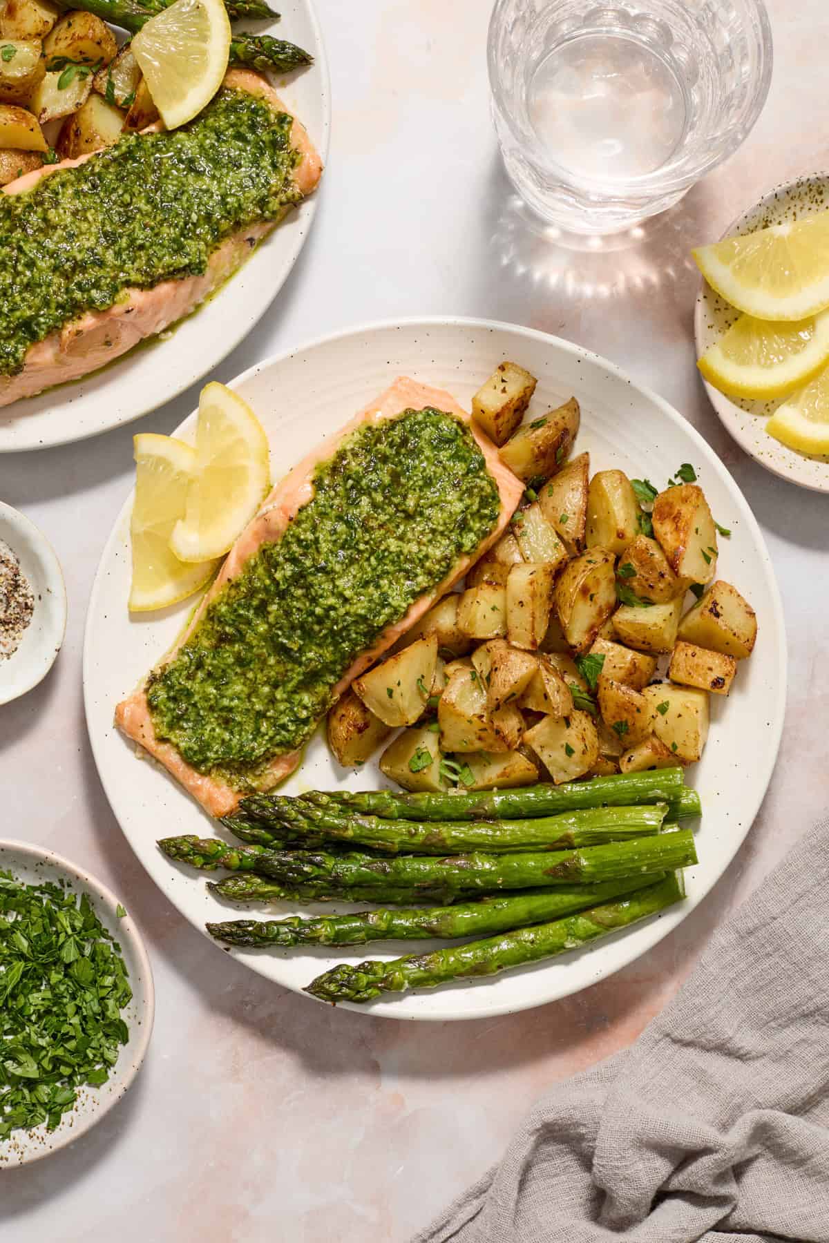 Pesto covered salmon on white plate with parmesan potatoes, asparagus and lemon slices.