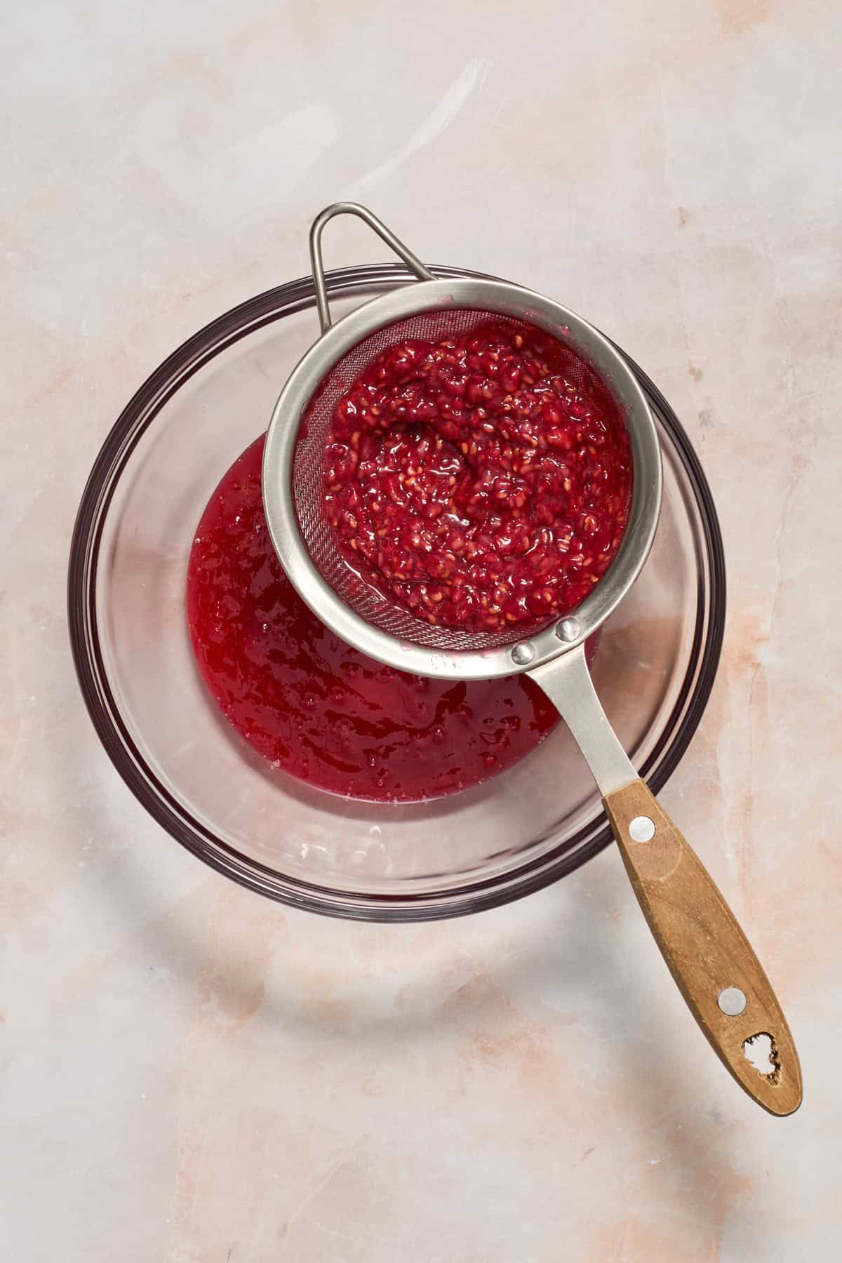 Raspberry seeds being separated from sauce in fine mesh sieve.