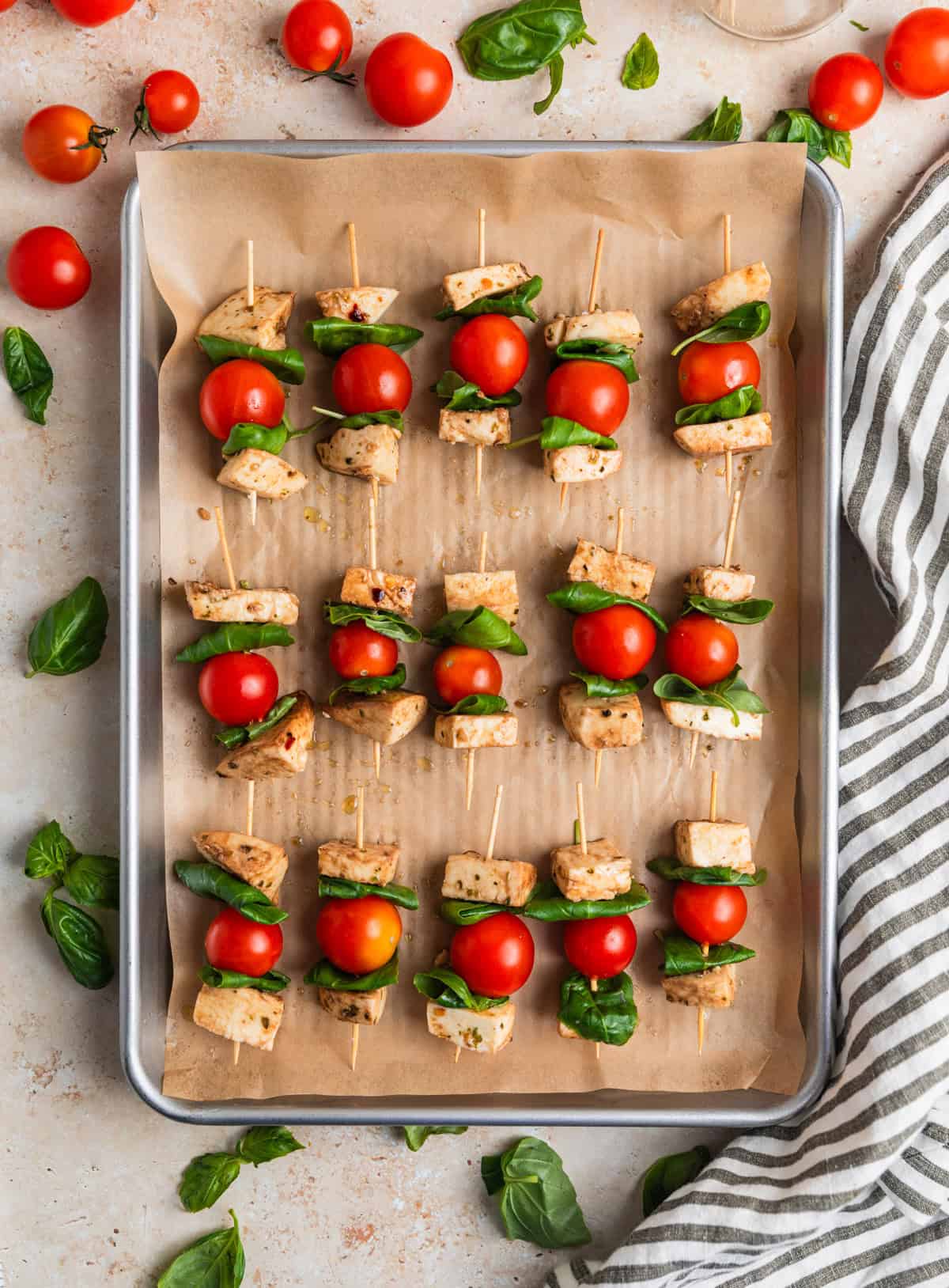 Skewers lined with grape tomatoes, basil leaves and marinated mozzarella on parchment lined cookie sheet.