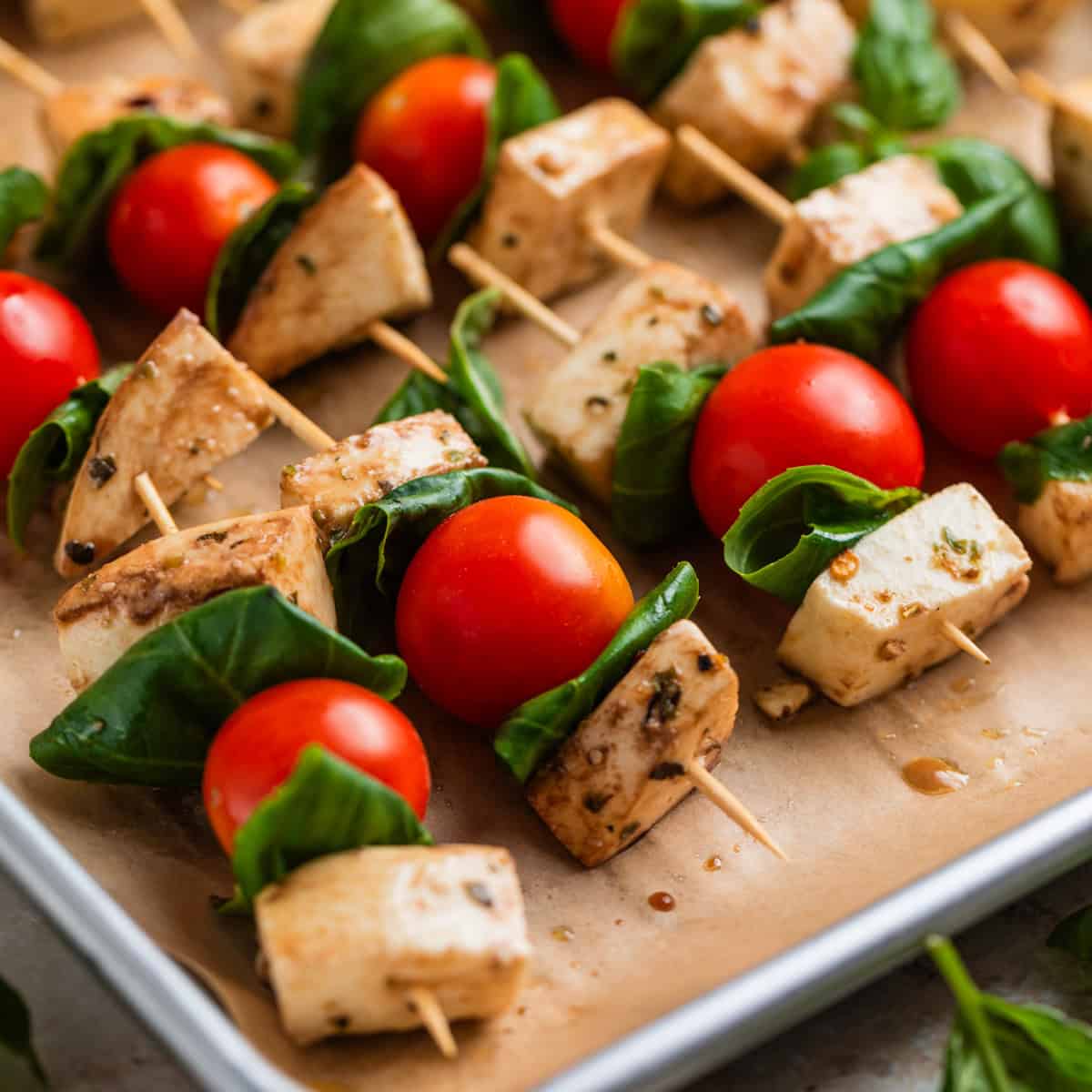 Tomato, basil mozzarella skewers lined up on parchment lined pan.