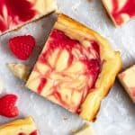 Overhead view of white chocolate cheesecake bars with raspberry swirl on wax paper.
