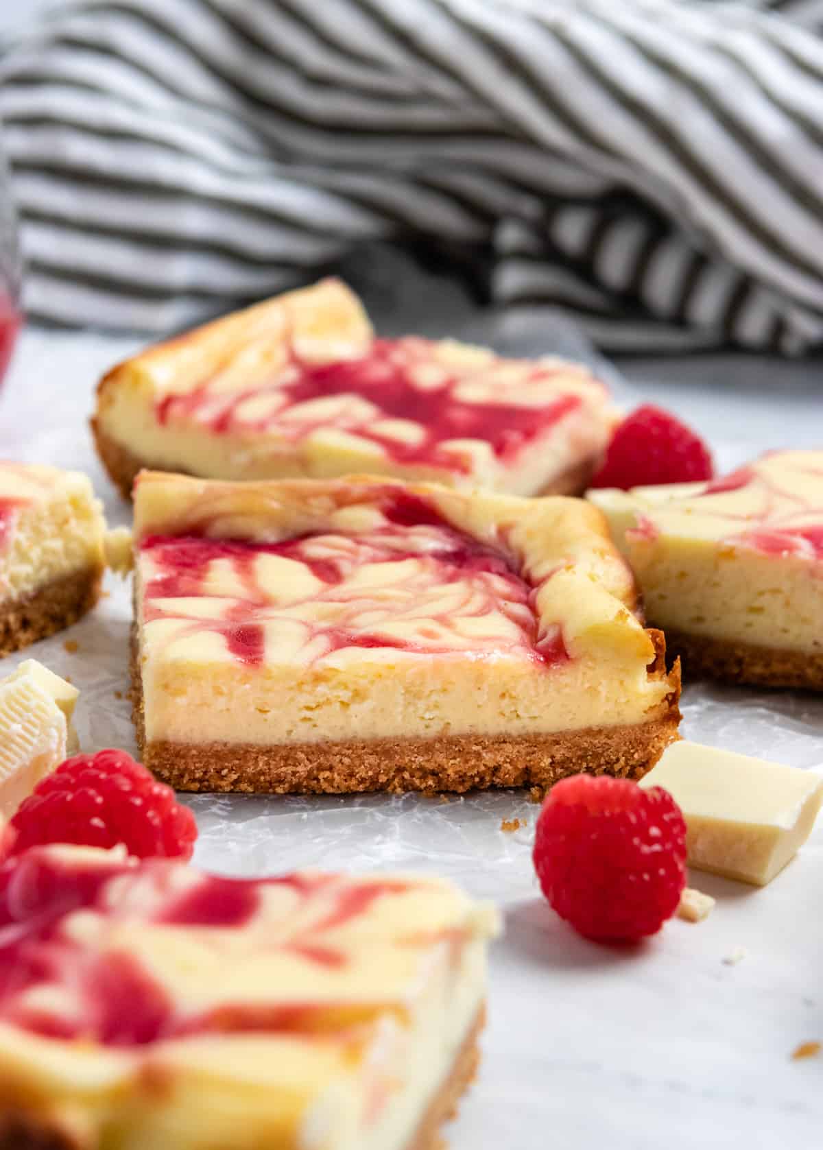 Raspberry white chocolate cheesecake bars on wax paper with fresh raspberries/