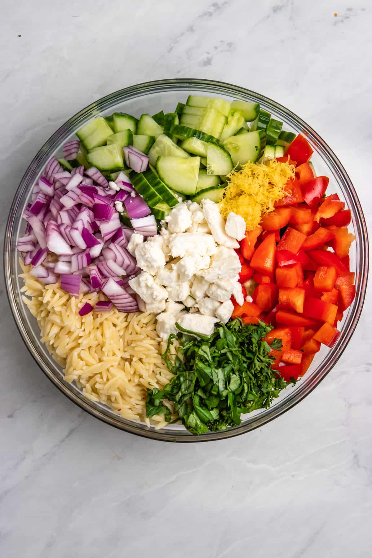 Overhead view of lemon orzo salad ingredients in mixing bowl.