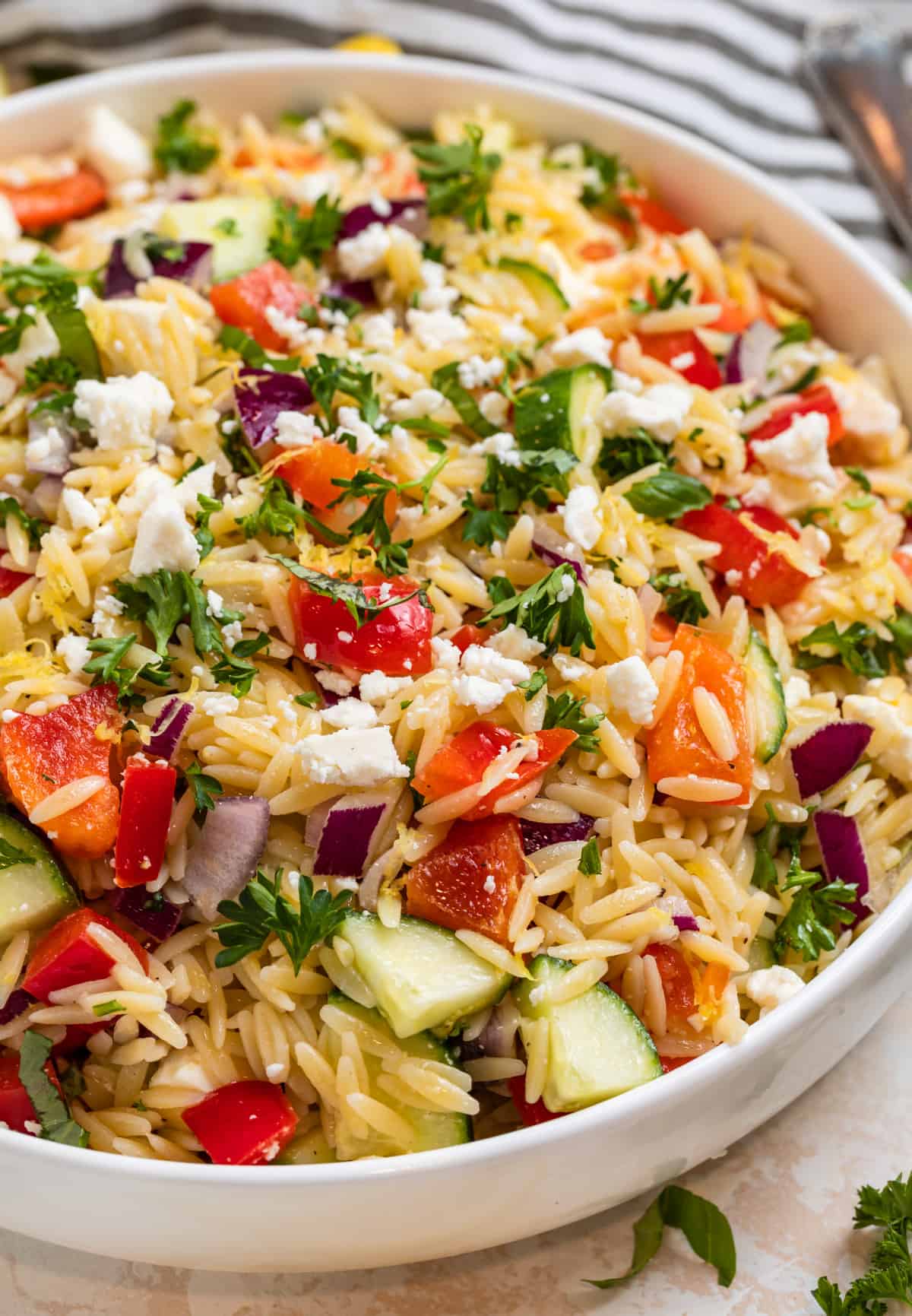 Orzo salad with feta, basil, parsley, cucumbers and more in white bowl.