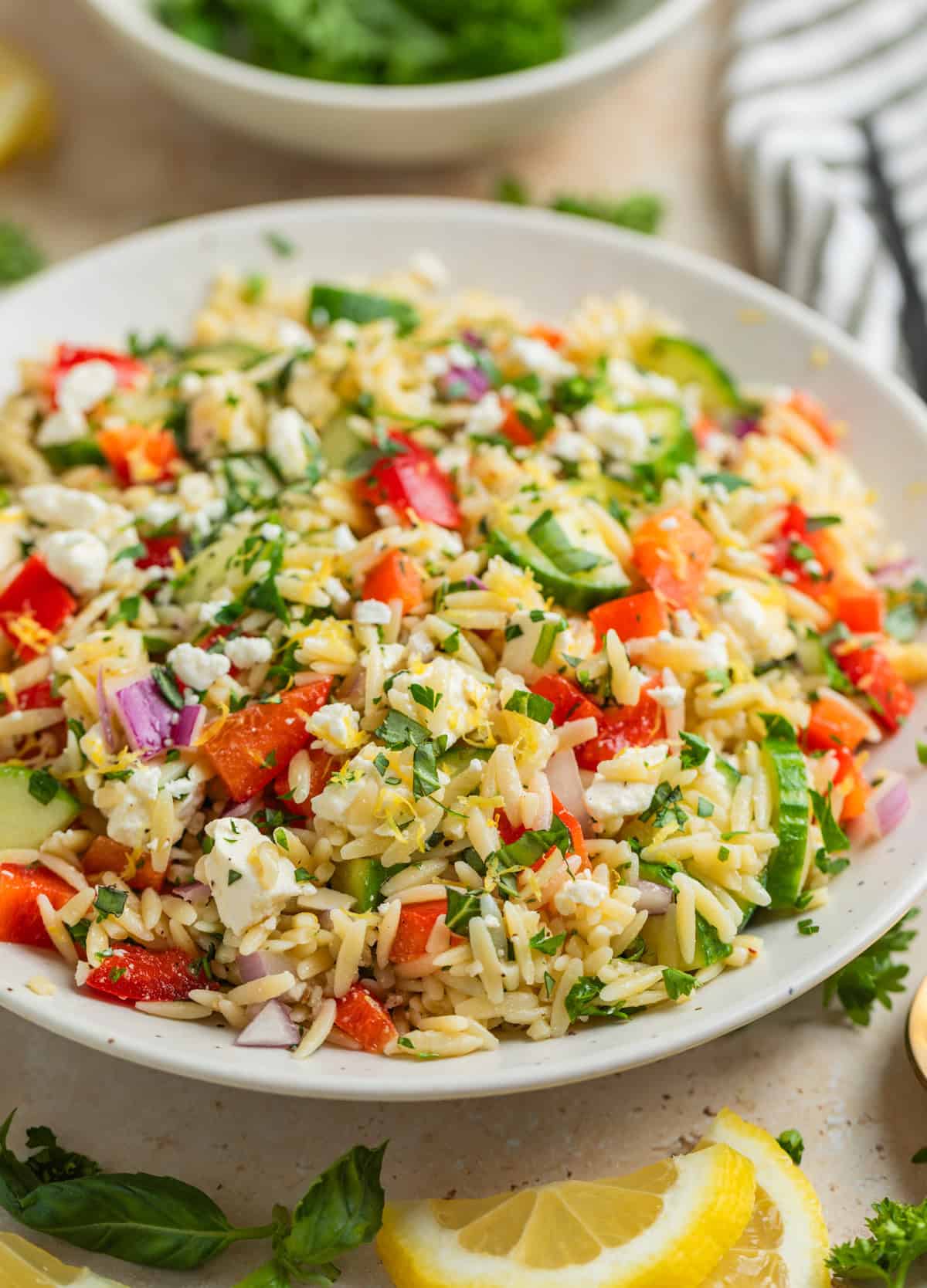 Orzo salad with feta, basil, parsley, cucumbers and more in white bowl.