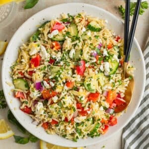 Lemon orzo salad with cucumber, bell pepper and feta in serving dish with serving utensils.