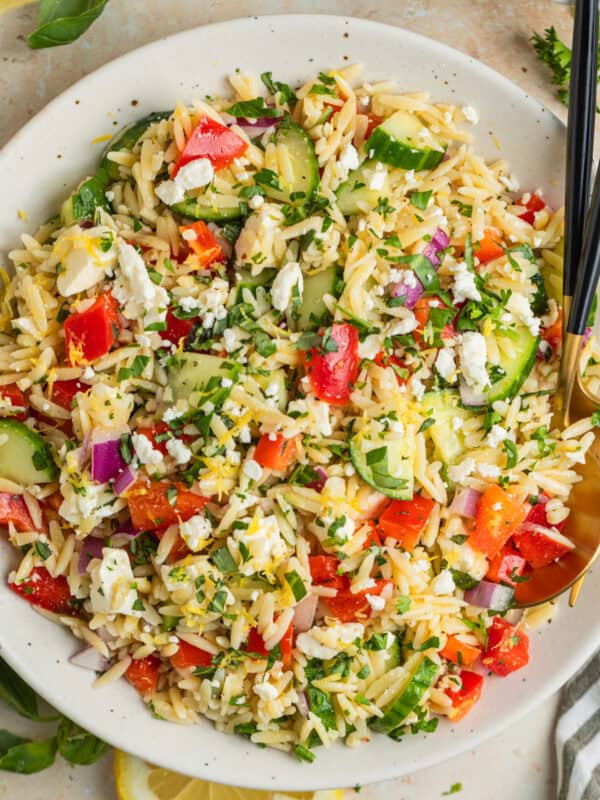 Lemon orzo salad with cucumber, bell pepper and feta in serving dish with serving utensils.