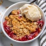Strawberry crumble in white bowl with ice cream and spoon.