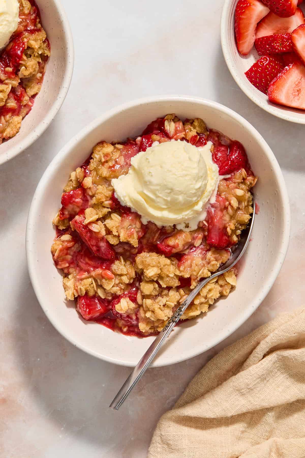 White dish with serving of strawberry crumble topped with vanilla ice cream.