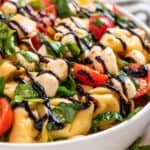 Tortellini caprese salad in bowl topped with balsamic glaze.