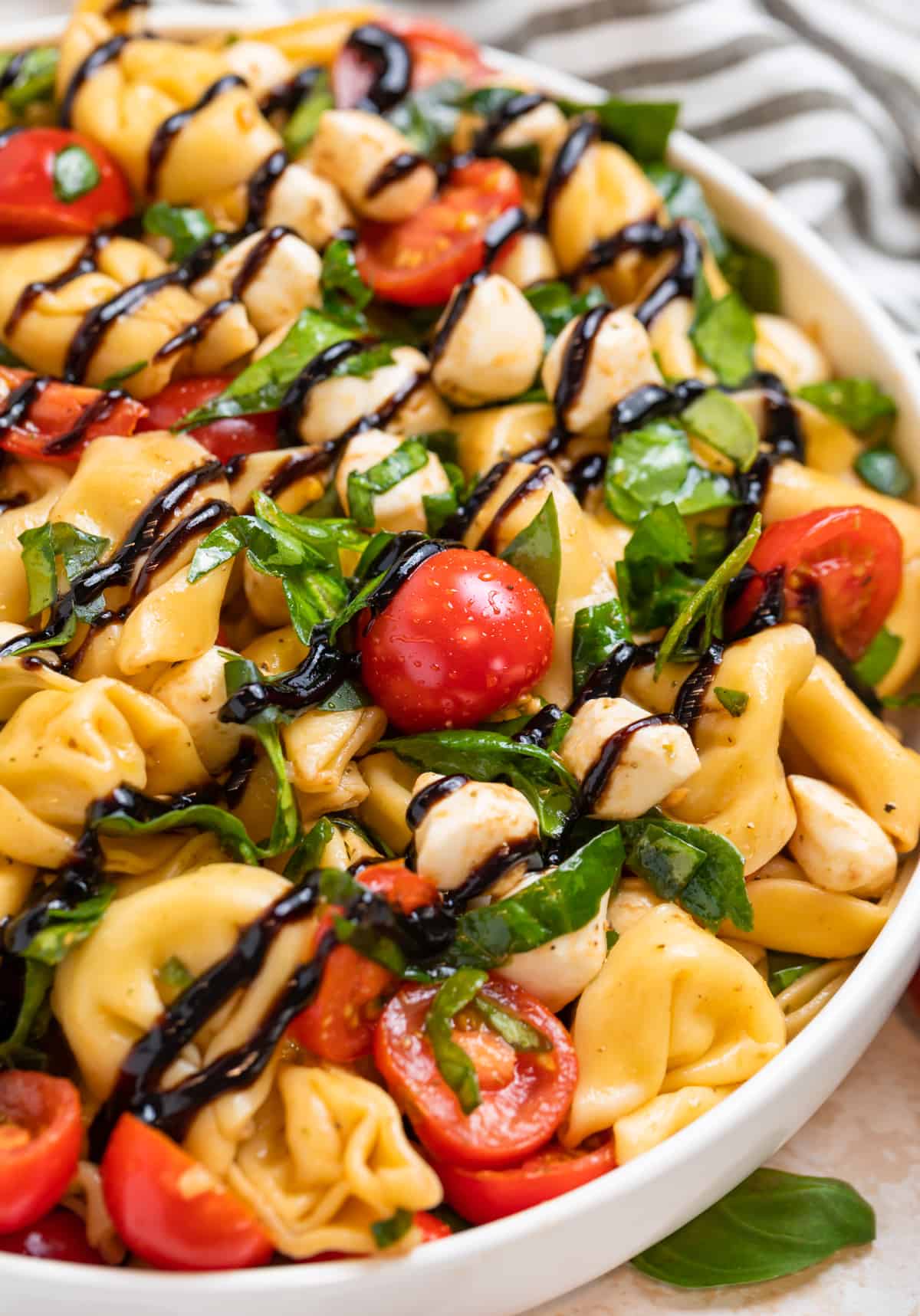 Tortellini pasta salad in white bowl with balsamic glaze drizzled on top.
