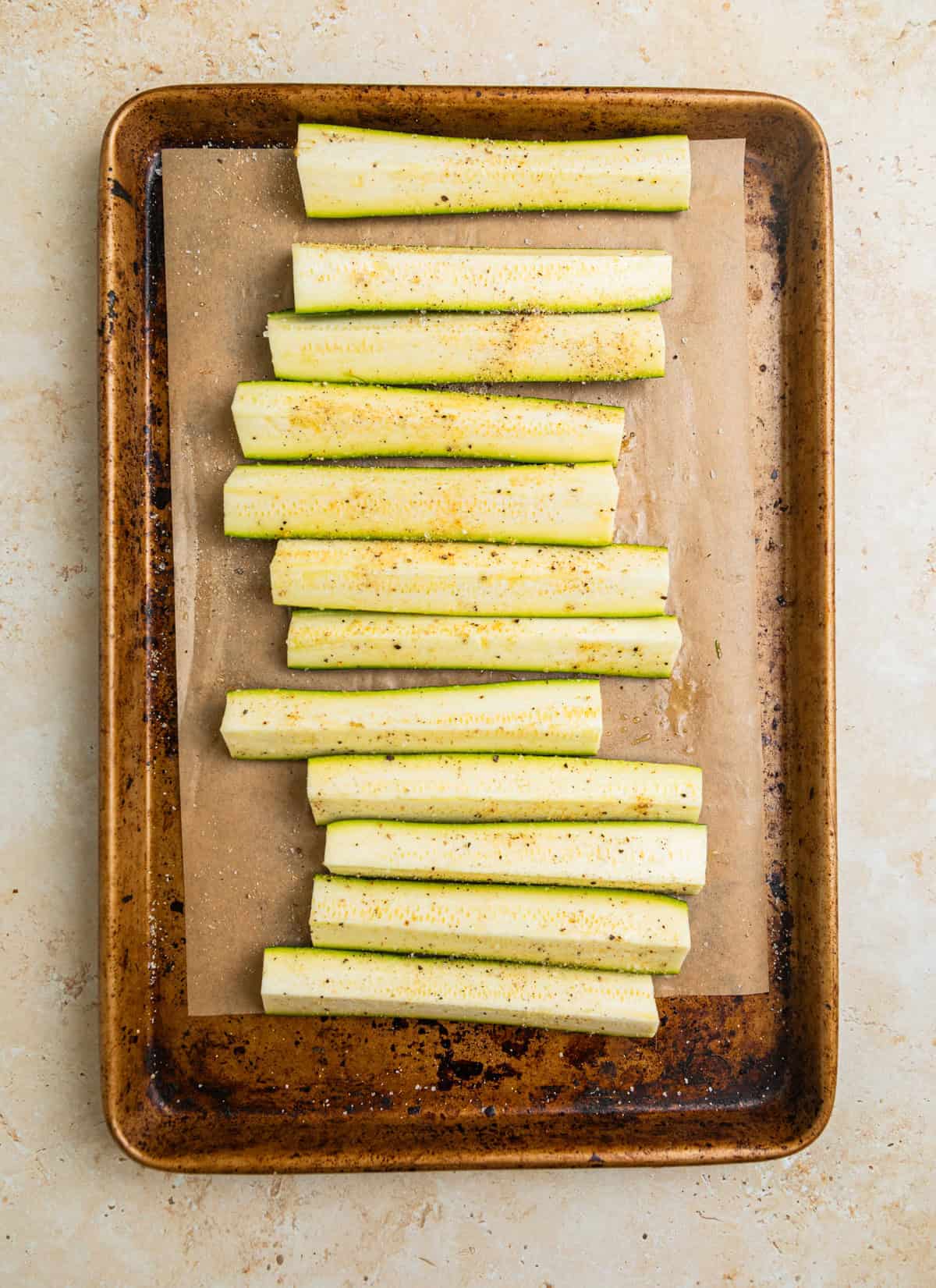 Seasoned zucchini pieces on parchment lined sheet pan.